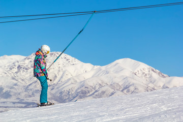 skier in equipment rises on a lift up the hill for skiing against the blue sky and mountain peaks.