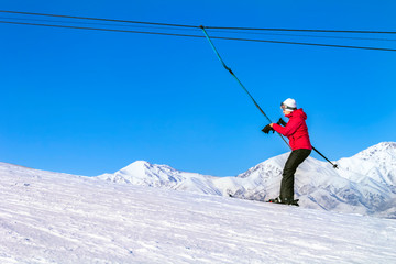 skier in equipment rises on a lift up the hill for skiing against the blue sky and mountain peaks.