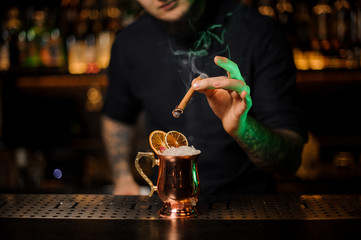 Bartender adding to a cocktail with dried orange a smoked cinnamon
