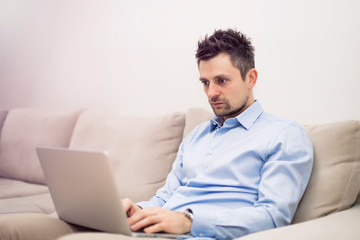 Upset and worried young businessman sitting and working at laptop