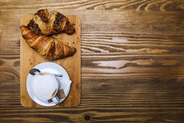 Cup of cappuccino coffee and croissants on a wooden table