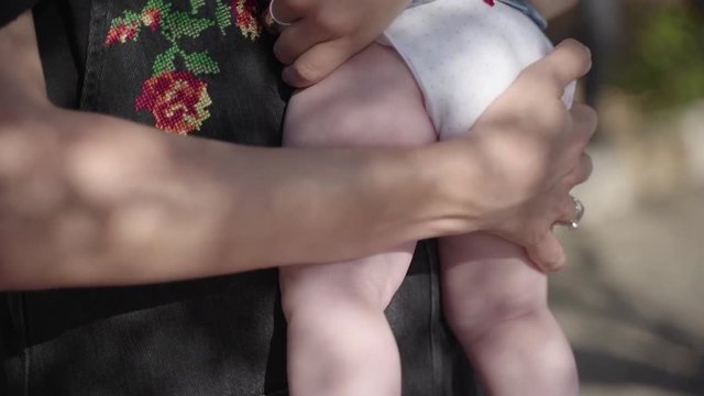 A close-up plan of a kid's legs, a mother holds on hands a little baby