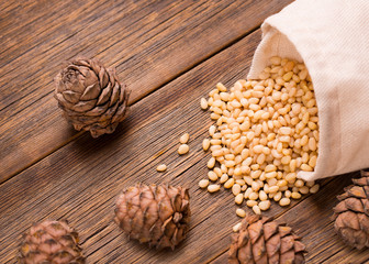 Peeled pine nuts are poured from a textile bag on a wooden table. Pine nut on a wooden background.