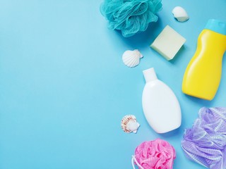 Still life bath products photo. Blue, pink and purple sponges, yellow shampoo bottle, shower gel, soap bar and seashells. Mockup with free space for text 