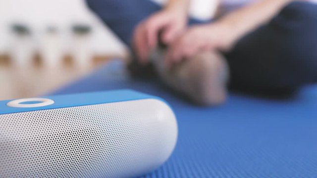 A woman sitting on the floor turns on a portable bluetooth speaker and listens to music with pleasure.