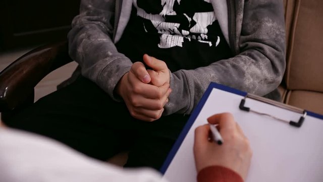 Young worried teenager at the psychologist for counseling - closeup on hands, camera slide and refocus