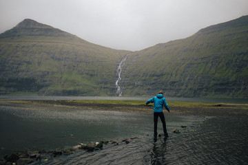 Man treading carefully over stones in a river on hike to reach waterfall in Faroe Islands 