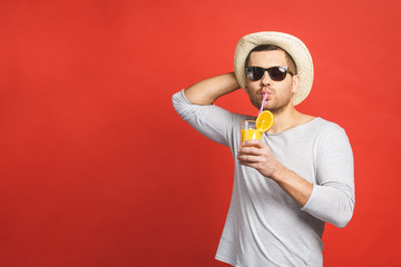 Happy holidays! Handsome young man in hat and sunglasses drinking fresh orange juice over red background.