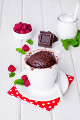 Chocolate mug cupcake with whipped cream, chocolate chips and fresh raspberries on a white wooden background.