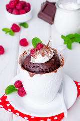 Chocolate mug cupcake with whipped cream, chocolate chips and fresh raspberries on a white wooden background.