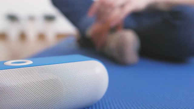 A woman sitting on the floor turns on a portable bluetooth speaker and listens to music with pleasure.