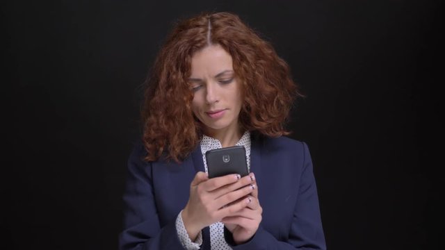 Closeup portrait of adult caucasian female with red curly hair viewing taken selfies on the phone then looking at camera