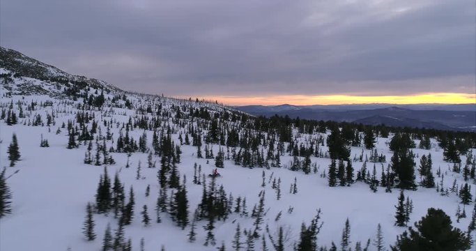a guy on a mountain snowmobile rides on the background of a beautiful sunrise in a forest mountain valley with fields of snow. snowmobile traffic in the mountains. stock video footage. Aerial shot