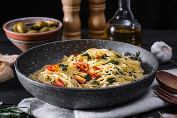 Pan of cooked italian pasta. Traditional spaghetti meal with vegetables and olives on black rustic background