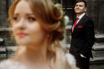 elegant wedding couple posing in old courtyard in european street. luxury bride under veil and groom looking at her. romantic sensual moment