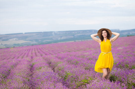 Beautiful relaxed smiling woman in yellow dress stratched hands in purple flower lavander field.
