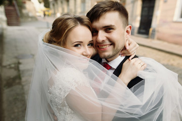 Naklejka premium Cheerful bride and groom hugging face closeup, newlywed couple smiling in embrace outdoors, family portrait concept