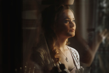 gorgeous bride portrait in the morning in room. unusual creative view through glass. happy stylish woman. wedding preparation.