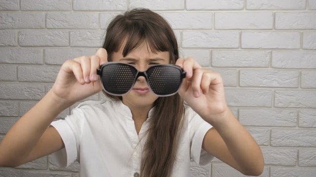 The child puts on glasses for training of sight. A little girl puts on obscura glasses.