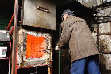 A man is a worker, pulls out the hot parts from an electric furnace for hardening metal. A man at dangerous work with high temperature in a heavy industry at the valve manufacturing plant