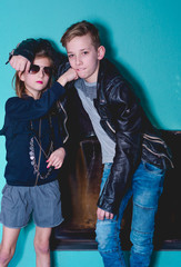 two children, boy and girl dressed in urban style on the background of a blue wall