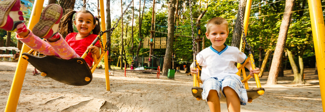 Sister and brother in playground swing outdoors - Powered by Adobe
