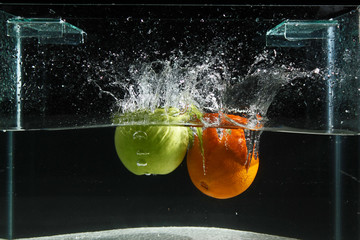 Apple and orange splashing into water on a black background, fishing tank exposed shooting in the studio doing photography tricks