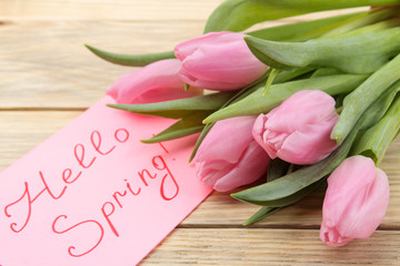 Beautiful bouquet of pink tulips flowers and text hello spring in notebook on natural wooden background.  Spring. holidays.