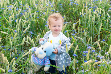 Little girl on a walk with her toy in a cornflower field.