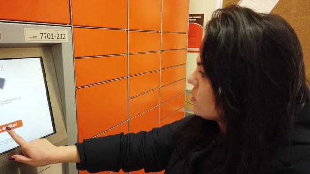 Girl receives a package in the mail postal terminal, he presses a button and the door of the cell opens, girl picks up the package
