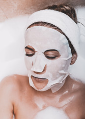 Woman with rejuvenating face mask in bathtube. Anti-wrinkles skin care.