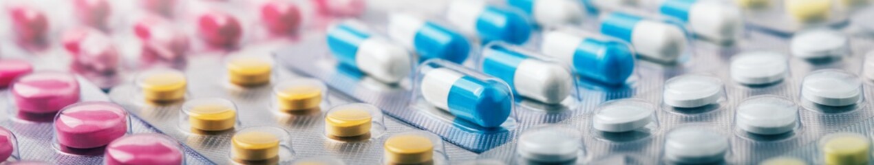 Heap of medical pills in white, blue and other colors. Pills in plastic package. Panoramic banner...