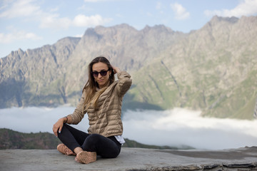 Fototapeta premium Young beautiful girl in a jacket with sunglasses against the background of the Caucasus Mountains in Georgia. Close-up