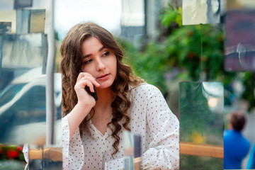 A young, sympathetic, dark-haired woman using a smartphone. Portrait of a woman through a mirror installation.