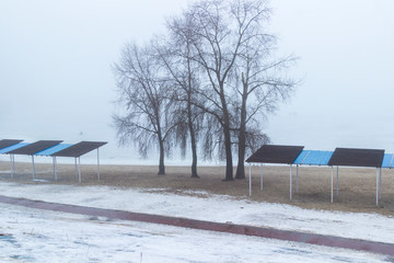 Empty beach in spring on the banks of the river, trees and shelter from the sun. Foggy