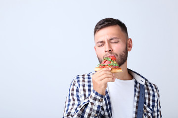 Young man eating pizza on grey background