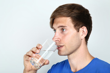 Beautiful young man drinking water on grey background