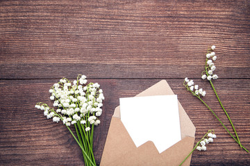 Lily of the valley flowers with envelope on wooden table