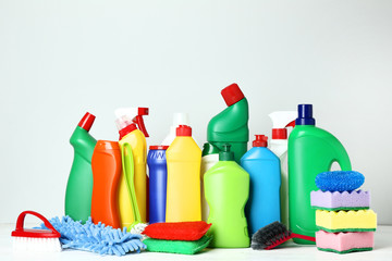 Bottles with detergent and cleaning tools on grey background