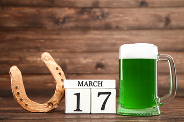 St. Patrick's Day. Green beer in mug with cube calendar and golden horseshoe on wooden background