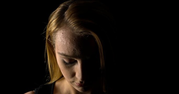 Woman abuse. Sorrow woman portrait in shadow, black background.