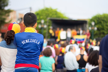 Young boy with Venezuelan pullover watching a stage at Venezuelan protest against Nicolas Maduro - obrazy, fototapety, plakaty