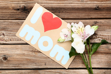 Greeting card with text I Love Mom and flowers on brown wooden table