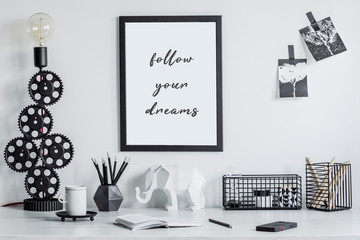Modern and stylish black and white home decor mock up. Creative desk with blank picture frame or poster, desk objects, office supplies, elephant figure and design table lamp on a white background.