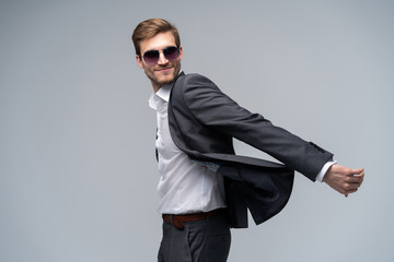 Feeling free and comfortable in his style. Handsome young man in full suit and sunglasses moving in front of gray background.