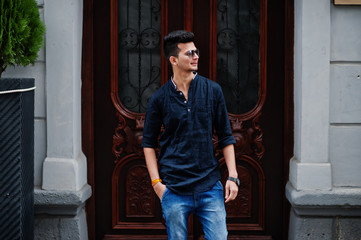 Stylish indian model man in casual clothes and sunglasses posed outdoor at street of India.