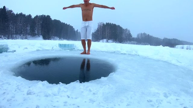 Young man with lean body jumps into the ice hole and haves recreational winter swim