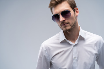 portrait of a young fashion man wearing sunglasses on grey background.