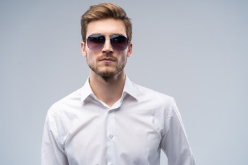 portrait of a young fashion man wearing sunglasses on grey background.