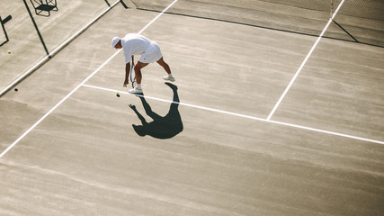 Senior man bending down to pick a tennis ball during a game of t